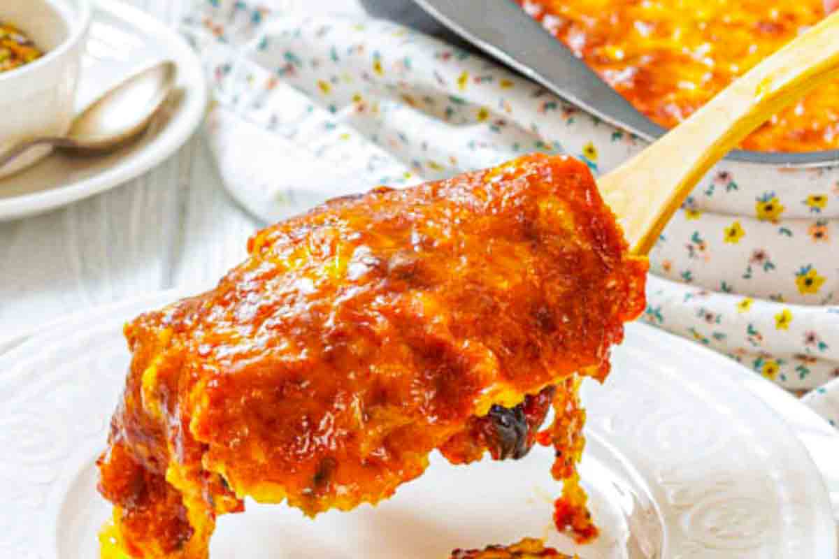 A serving of cheesy, baked aubergine being lifted from a plate with a spatula, showing melted cheese and tomato sauce.