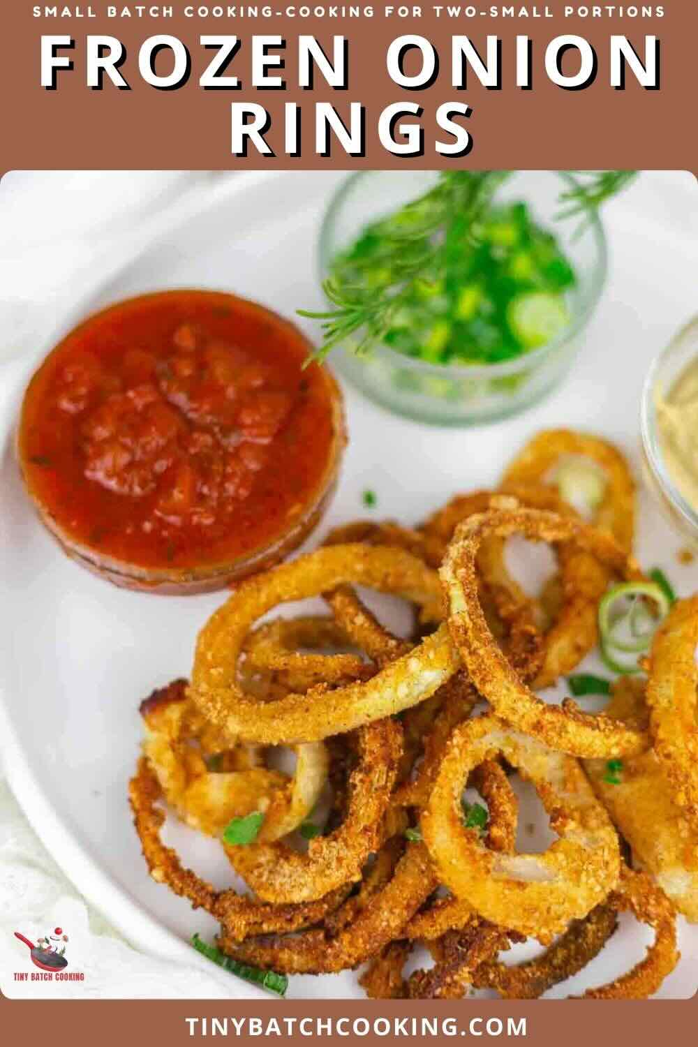 Plate of crispy frozen onion rings with a small bowl of tomato sauce, a bowl of chopped green onions, and a sprig of rosemary on a white plate.
