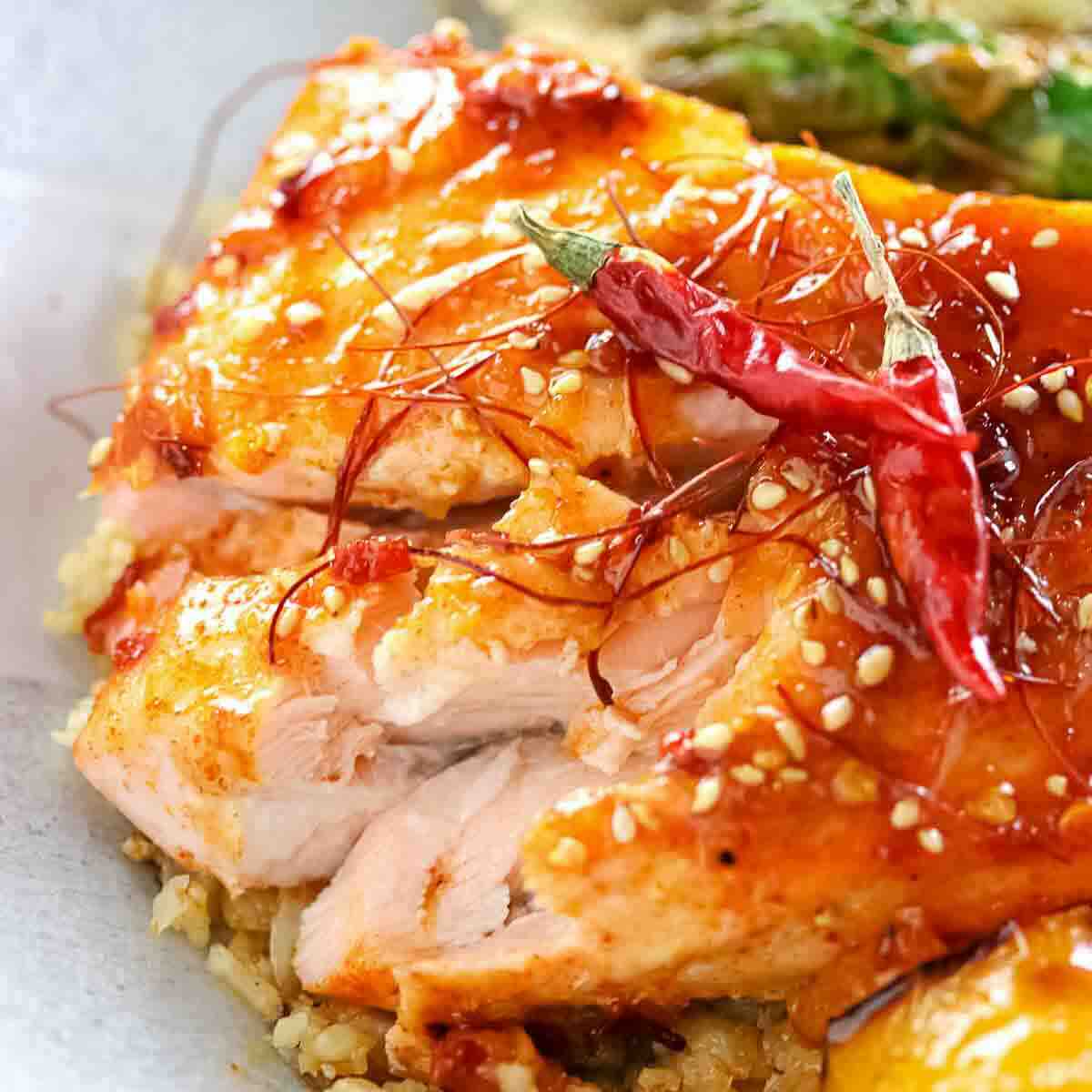 Close-up of cooked salmon fillet topped with red chili peppers, chili threads, and sesame seeds, served on a bed of grains.