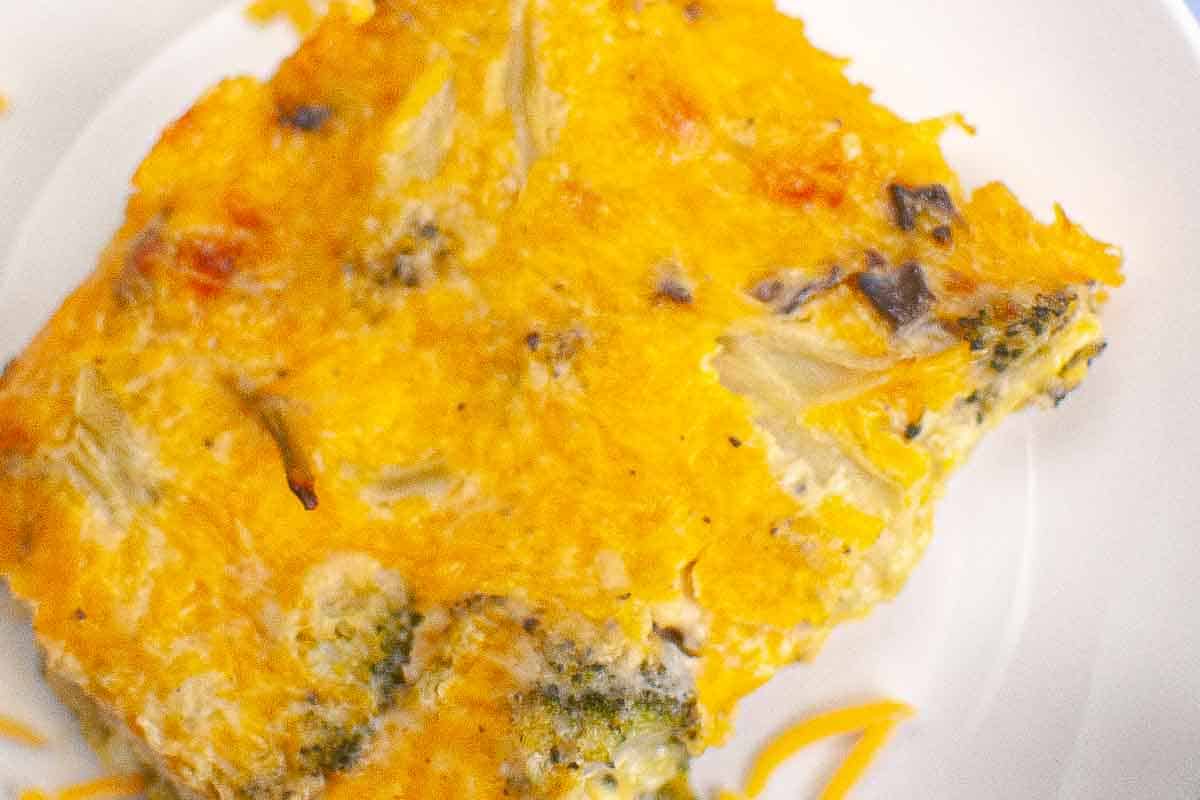 A close-up of a baked casserole slice with visible pieces of broccoli and cheese on a white plate.
