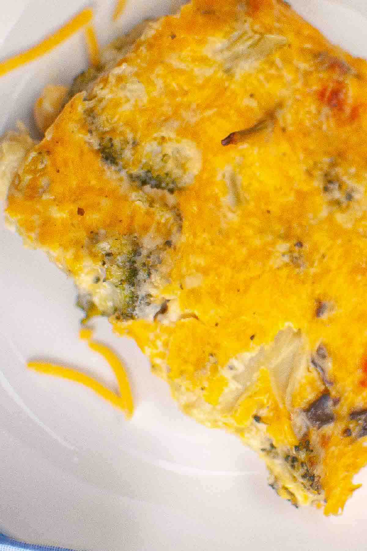 A slice of baked egg casserole with visible broccoli and melted cheese on a white plate.