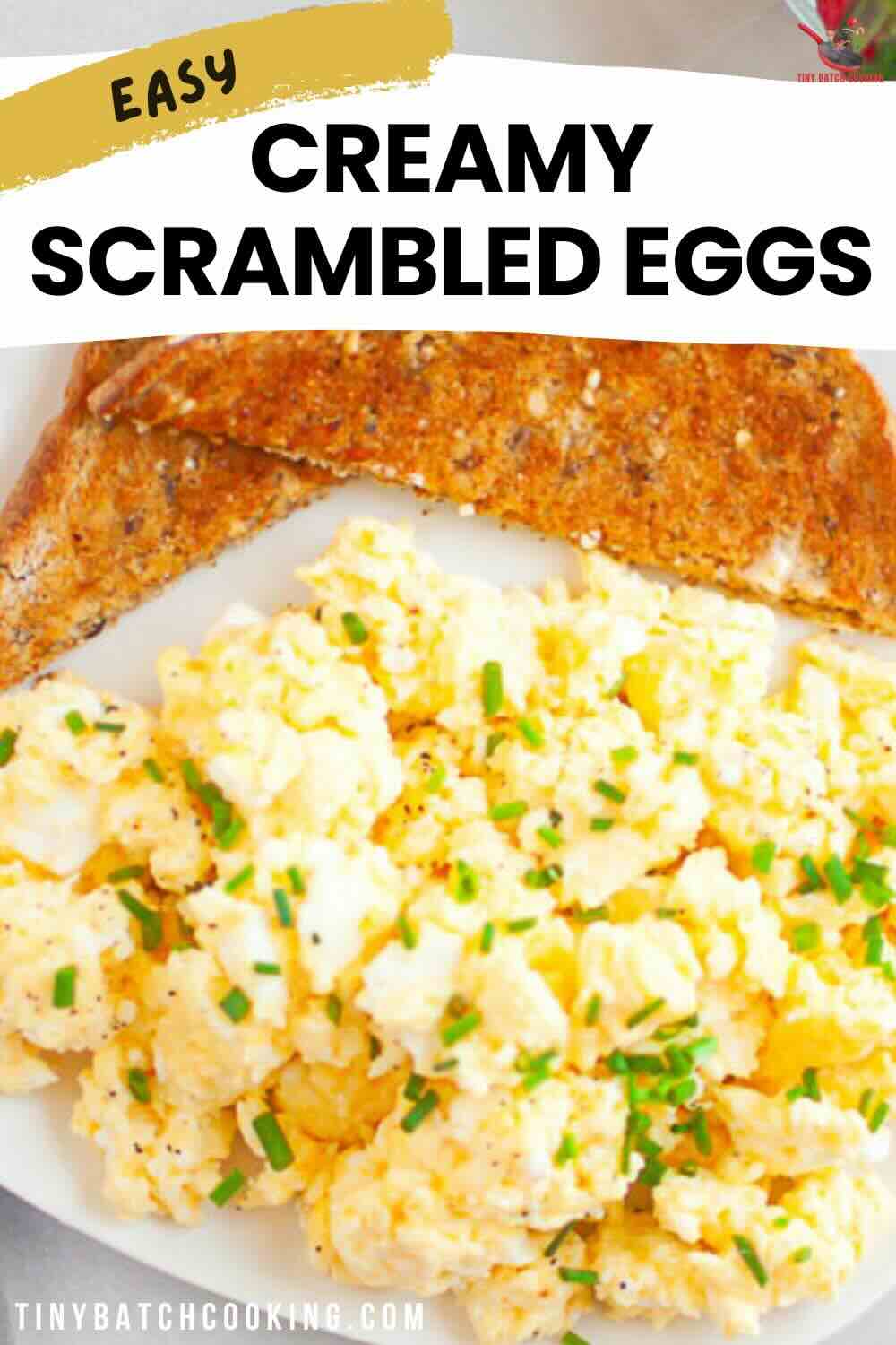 A plate of creamy scrambled eggs garnished with chopped chives, served with two slices of toasted brown bread.