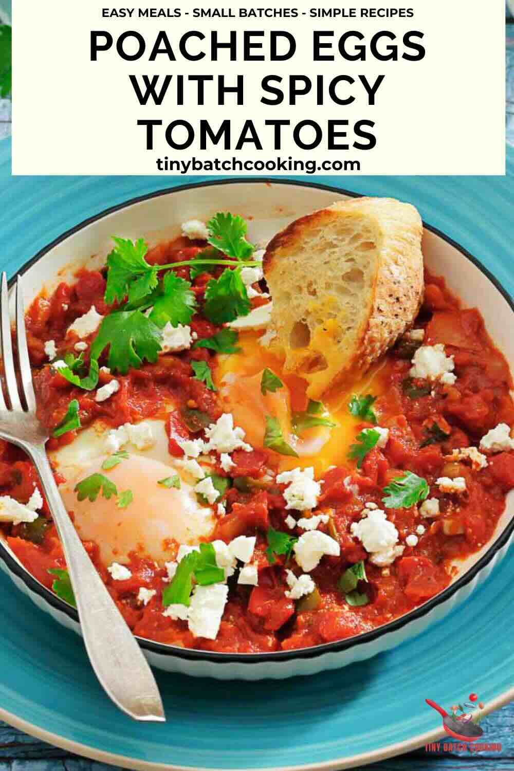 A plate of poached eggs in a spicy tomato sauce, garnished with cilantro and feta, served with a slice of crusty bread; a fork rests on the plate.