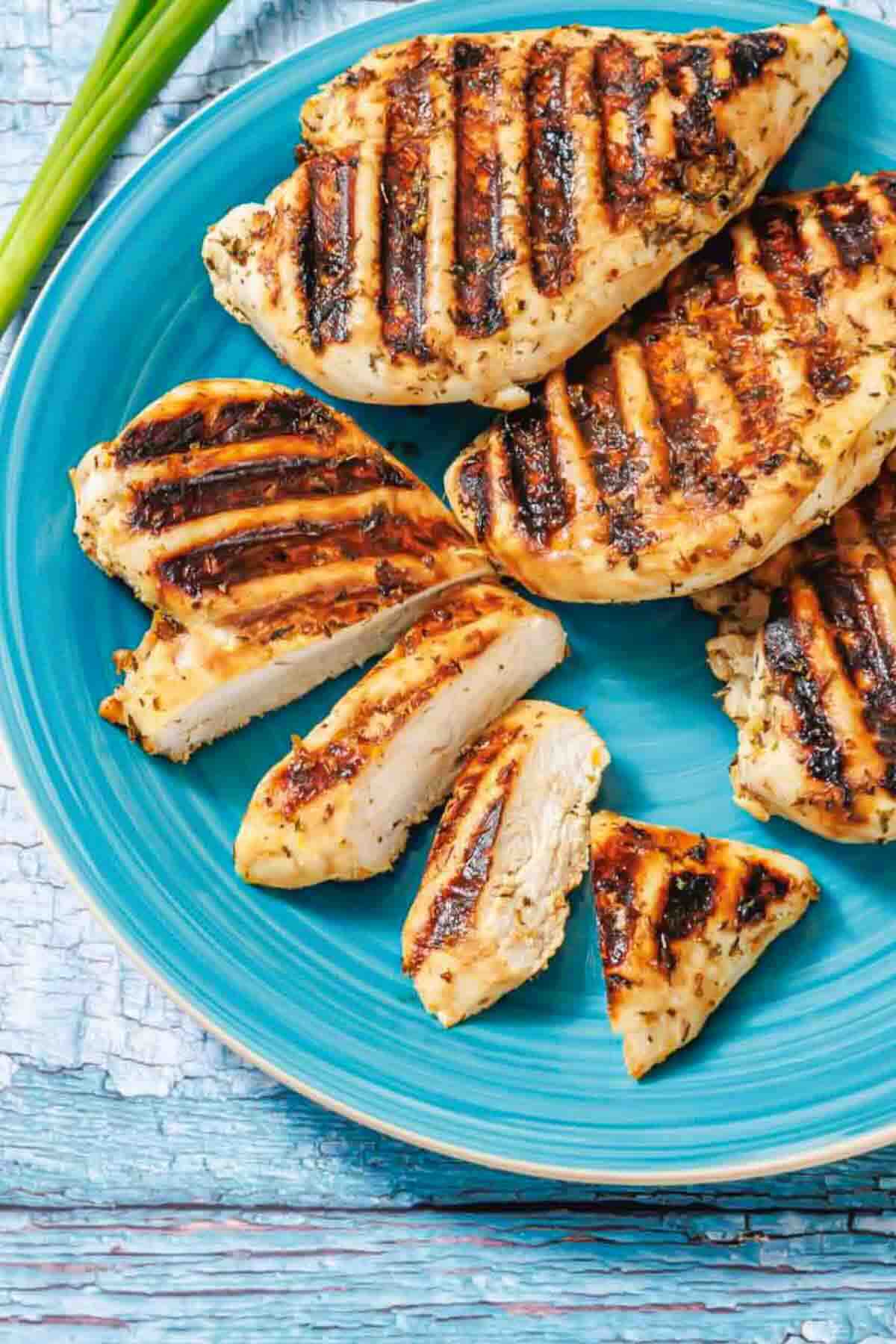 Grilled chicken breasts with grill marks, some sliced, served on a blue plate.
