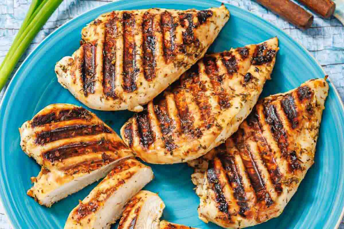 Grilled chicken breasts with visible grill marks arranged on a blue plate, some pieces sliced to show the cooked interior.
