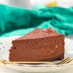A slice of chocolate cheesecake on a white plate with a gold fork, set in front of a green cloth.