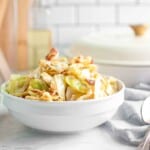 A white bowl filled with cooked cabbage, sliced sausage, and bacon pieces on a light-colored kitchen countertop.