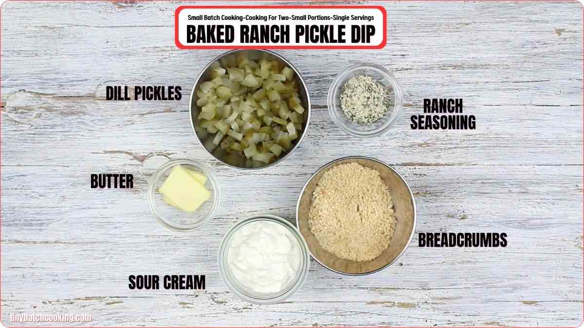 Five ingredients for baked ranch pickle dip—diced dill pickles, ranch seasoning, breadcrumbs, butter, and sour cream—arranged in bowls on a wooden surface with labels.
