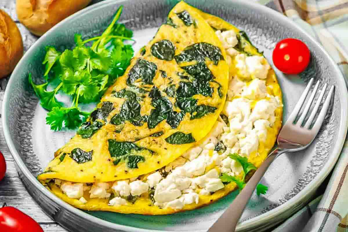 A spinach and feta cheese omelette is served on a gray plate with fresh cilantro and cherry tomatoes, next to a fork.