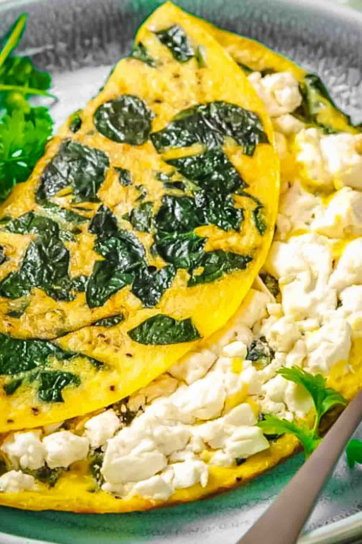 A spinach and feta omelette folded in half on a plate, garnished with fresh parsley.