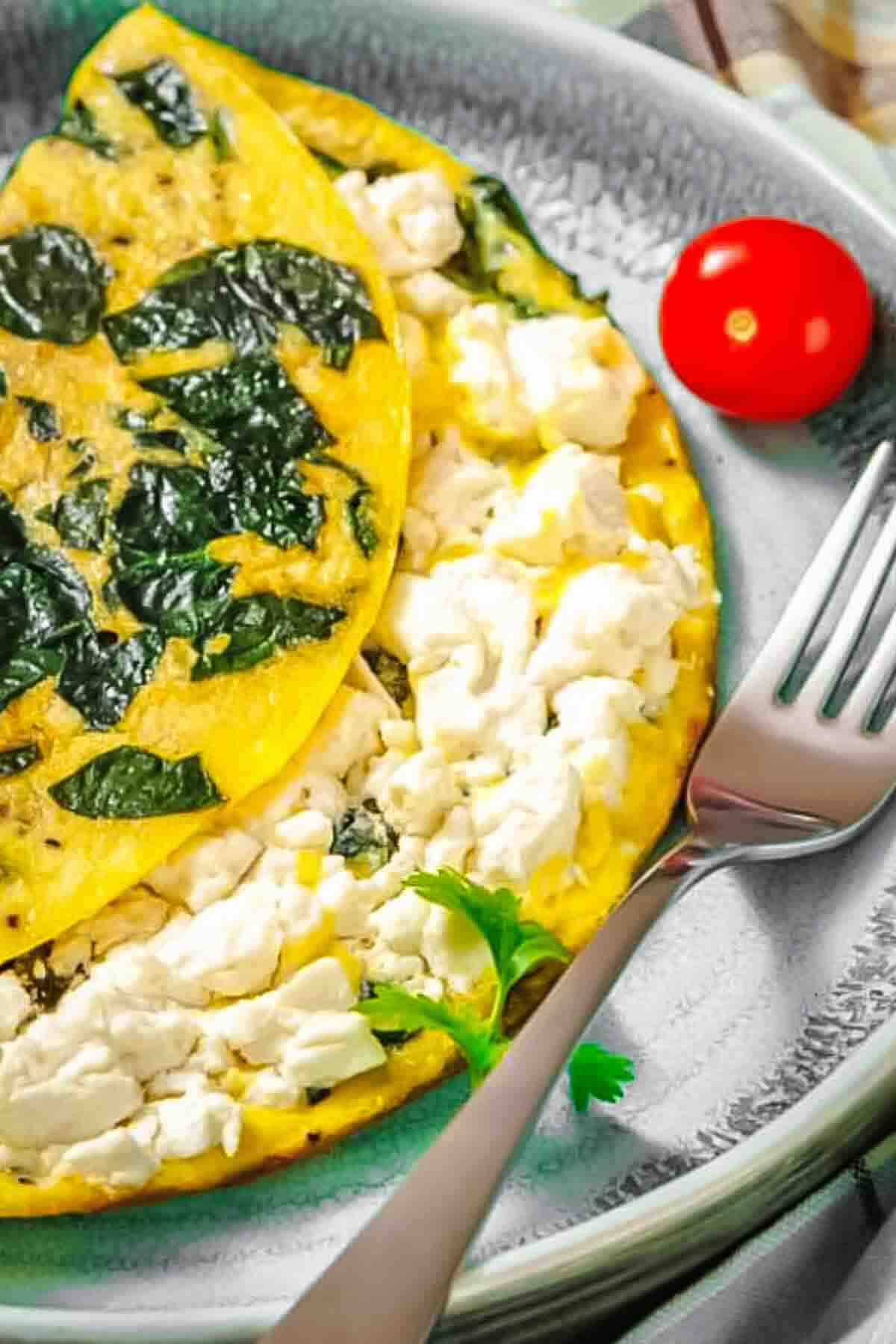 A spinach and feta omelette folded on a plate, garnished with a sprig of parsley, with a cherry tomato and fork beside it.