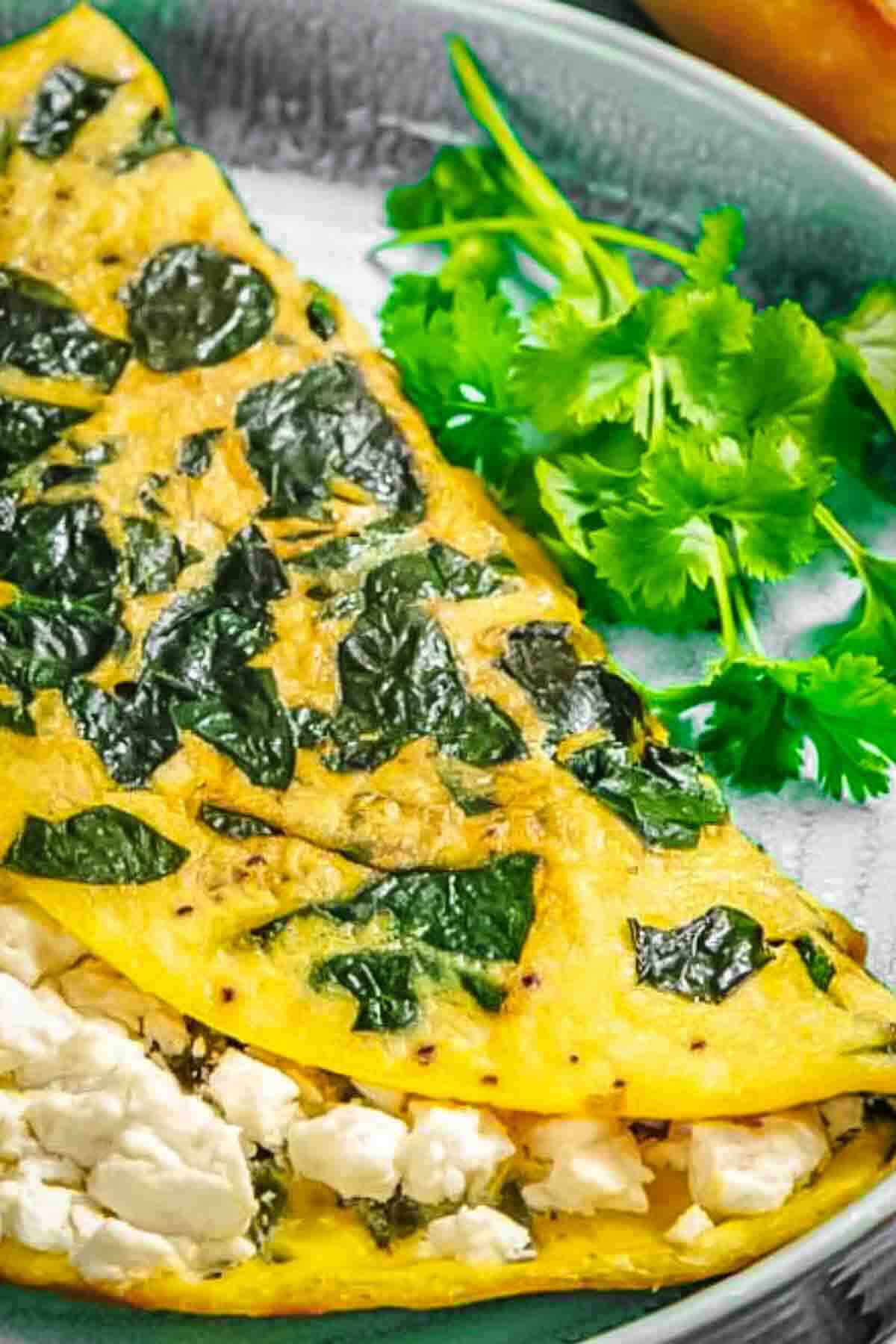 A spinach omelette filled with crumbled cheese, served on a plate with a side of fresh cilantro.