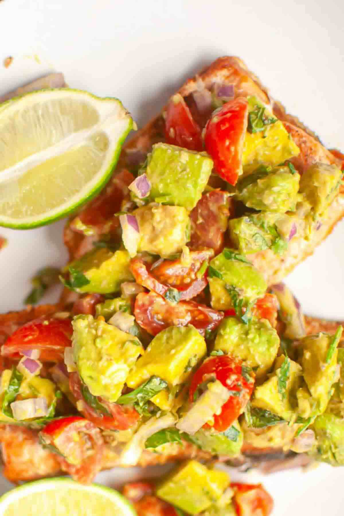 Close-up of toast topped with diced avocado, cherry tomatoes, red onion, and herbs, with a lime wedge on the side.