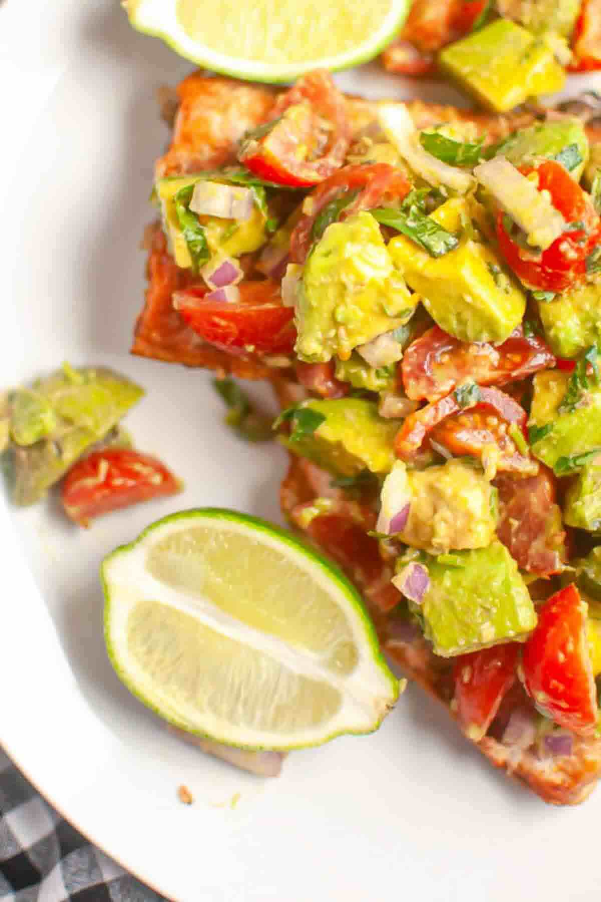 Close-up of avocado and tomato salsa on toasted bread, served with lime wedges on a white plate.