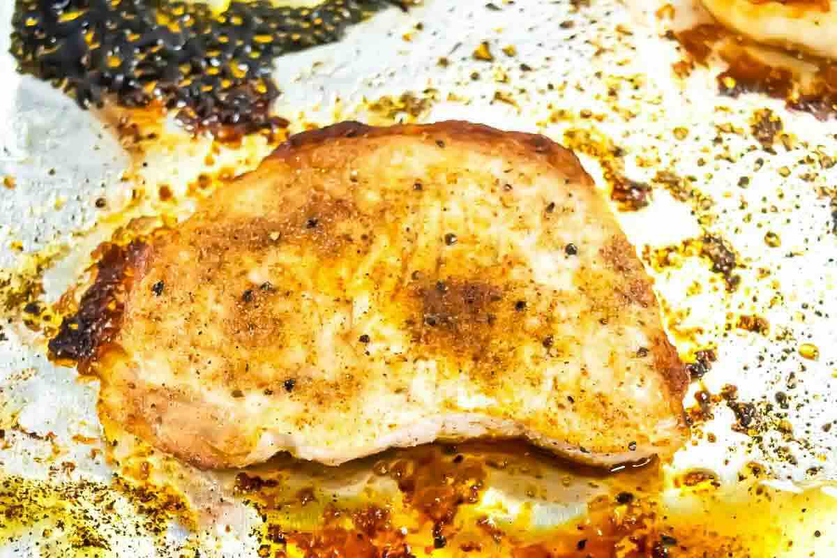Seasoned and cooked pork chop on a sheet pan with oil and spices, with some burnt residue visible on the foil.