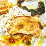 Cooked chicken breast with seasoning sits on a greasy, foil-lined baking sheet with burnt oil and baked residue visible around it.