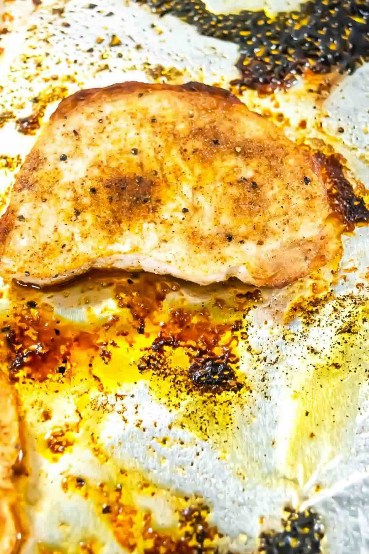 Cooked, seasoned chicken breast on a foil-lined baking sheet with visible oil and browned seasoning.