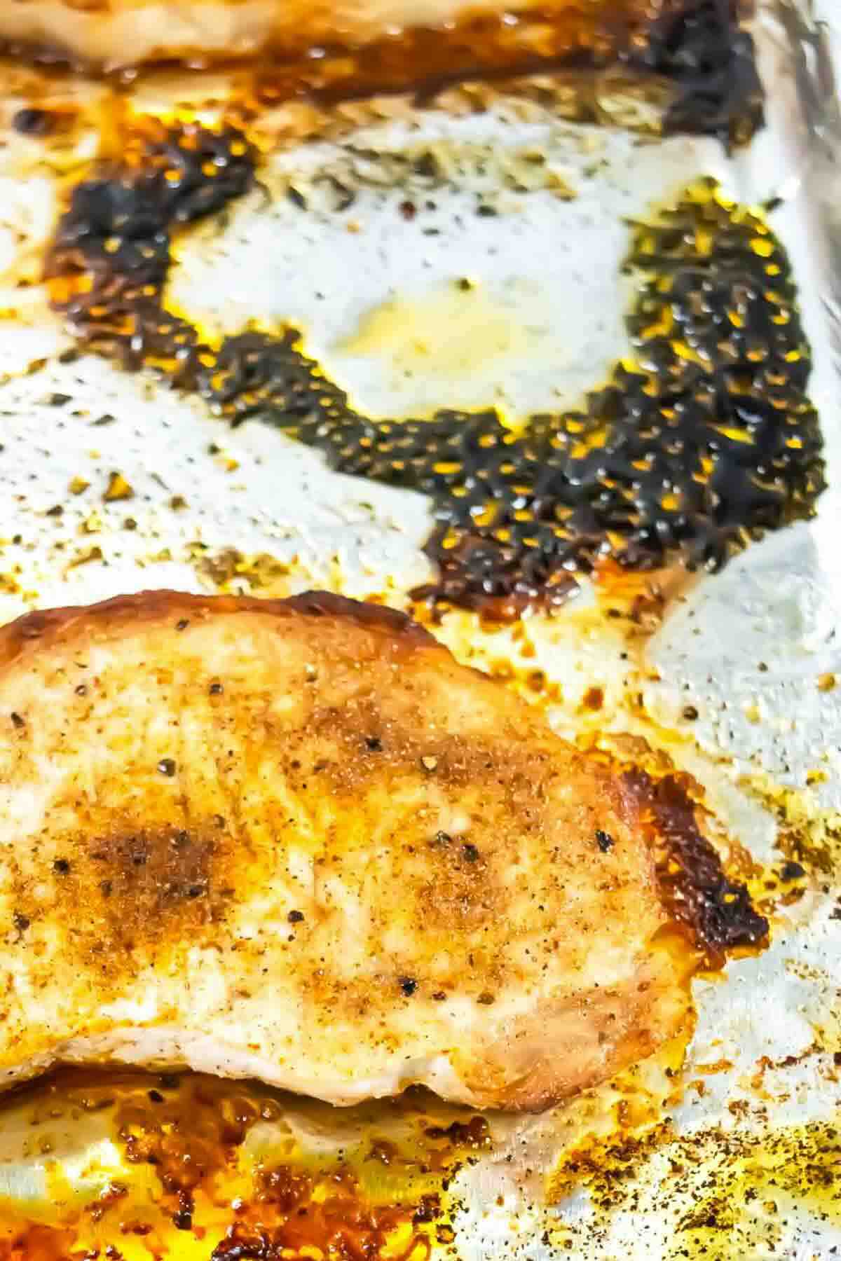A baked, seasoned chicken breast on a foil-lined tray with burnt seasoning residue and oil stains visible around it.