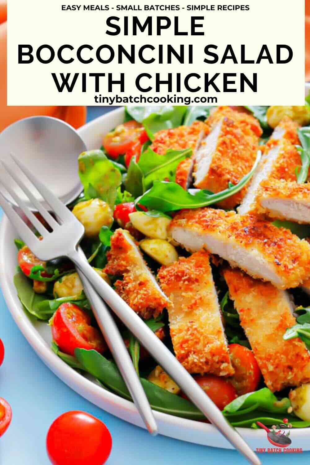 A plate of bocconcini salad with cherry tomatoes, leafy greens, and sliced breaded chicken, with a fork and knife on the side.