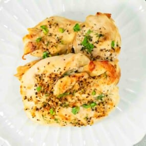 Two baked chicken breasts garnished with chopped herbs and cracked black pepper, served on a white plate.