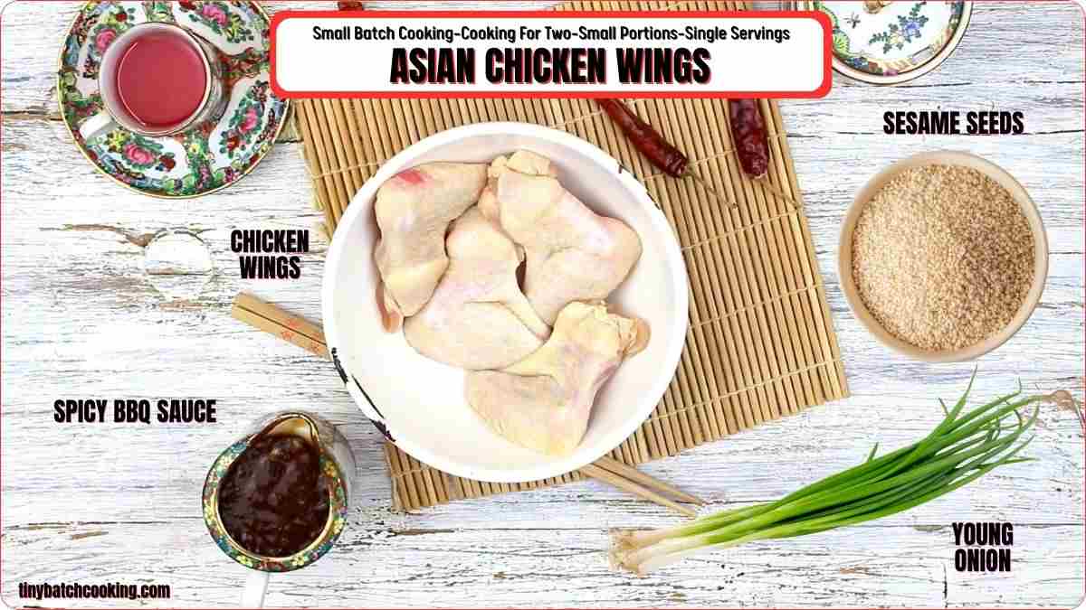 Raw chicken wings in a bowl, surrounded by bowls of spicy BBQ sauce, sesame seeds, sliced young onion, and dried red chilies on a bamboo mat with recipe labels.