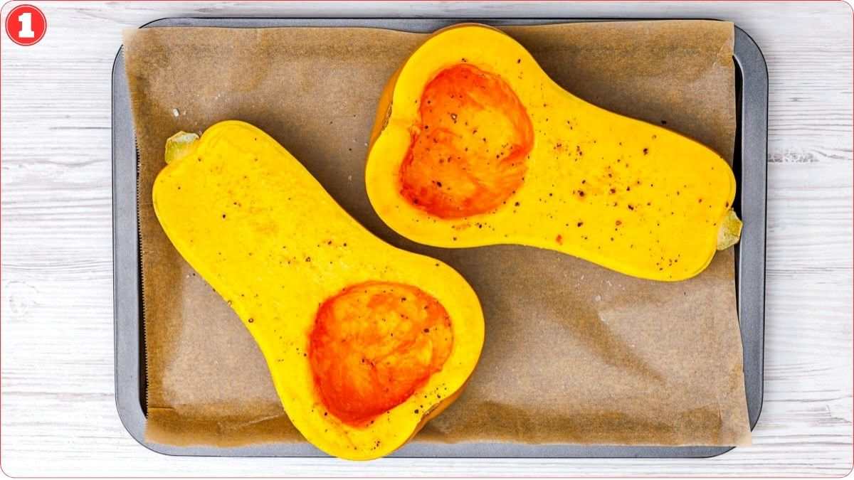 Two halves of butternut squash, seeded and seasoned, rest on a parchment-lined baking sheet.