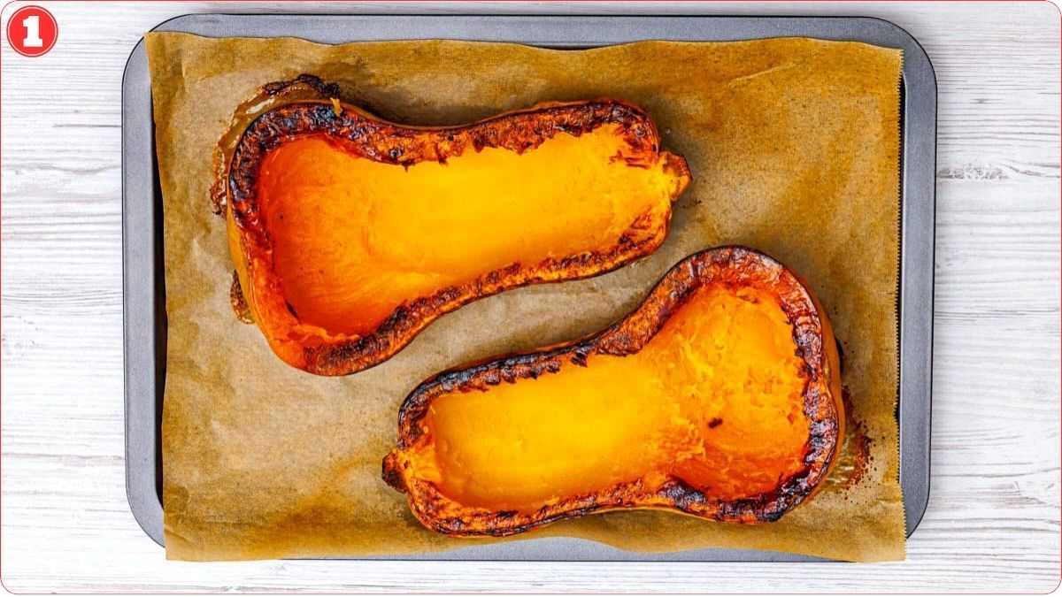 Two roasted butternut squash halves on a parchment-lined baking tray, with browned edges and soft orange flesh visible.