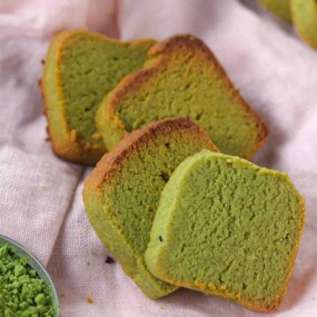 Three slices of green matcha pound cake on a cloth, next to a small bowl of matcha powder.